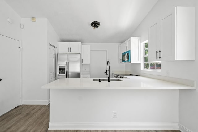 kitchen featuring stainless steel appliances, a sink, a peninsula, light countertops, and white cabinets