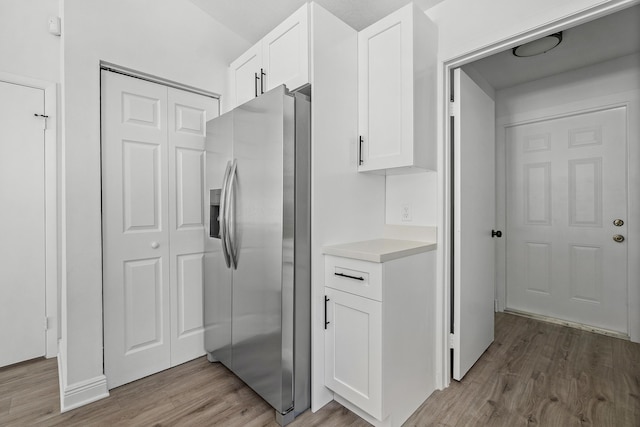 kitchen with stainless steel fridge with ice dispenser, light wood finished floors, white cabinetry, and light countertops
