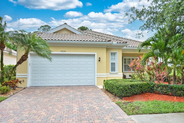 mediterranean / spanish house featuring decorative driveway, stucco siding, a garage, and a tiled roof