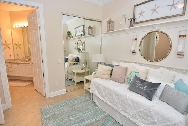 bedroom with light tile patterned floors, crown molding, a closet, a sink, and connected bathroom