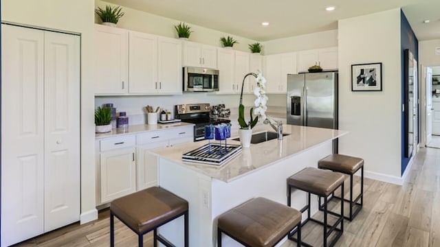 555 SE Rivergrass St, Port Saint Lucie, FL 34984 - kitchen with stainless steel appliances, white cabinets, light wood finished floors, a breakfast bar, and a center island with sink