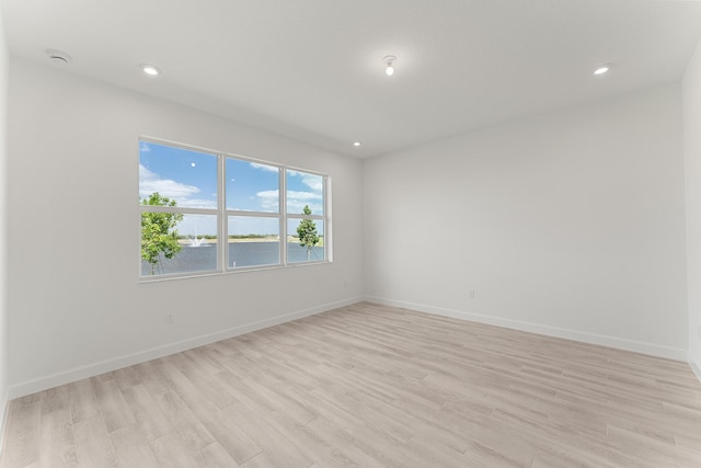 unfurnished room with light wood-style floors, baseboards, recessed lighting, a water view, and a smoke detector