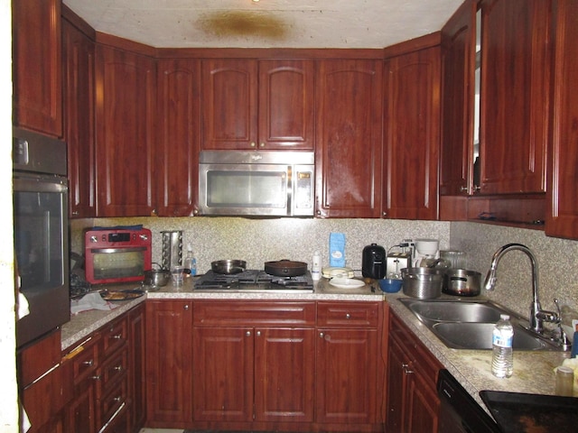 kitchen featuring appliances with stainless steel finishes, dark brown cabinets, a sink, backsplash, and light stone countertops