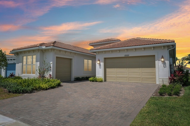 mediterranean / spanish house featuring an attached garage, a tile roof, stucco siding, and decorative driveway