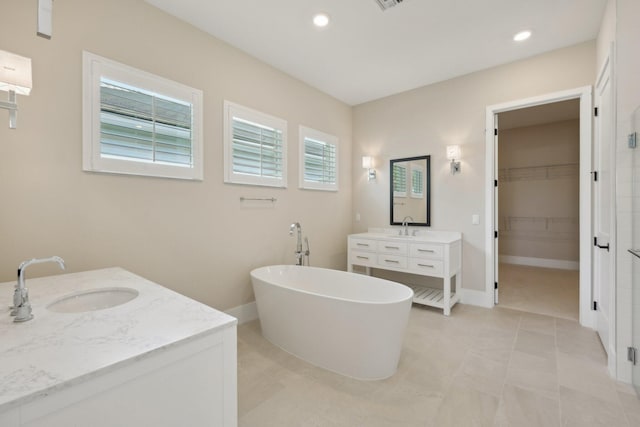 full bathroom featuring two vanities, a freestanding tub, a spacious closet, baseboards, and recessed lighting