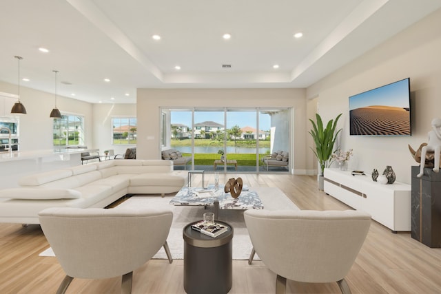 living room with a tray ceiling, light wood finished floors, and recessed lighting