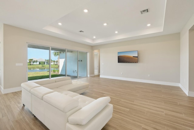 living room with a raised ceiling, baseboards, recessed lighting, and light wood finished floors