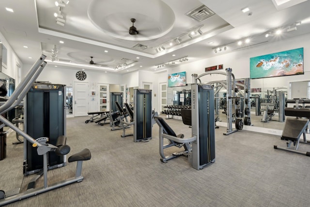 exercise room with ceiling fan, a raised ceiling, and carpet