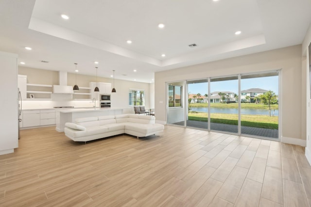 living room with a raised ceiling, recessed lighting, light wood-style flooring, and a water view