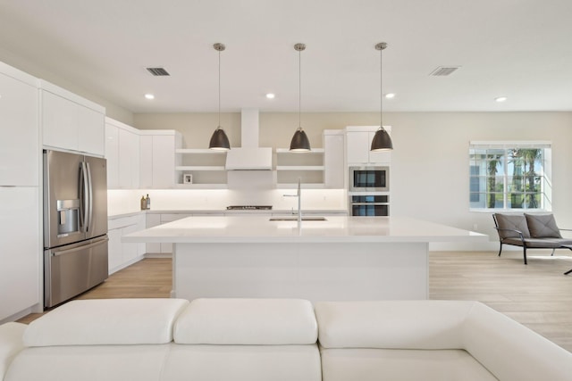kitchen with stainless steel appliances, open shelves, wall chimney exhaust hood, light wood finished floors, and light countertops