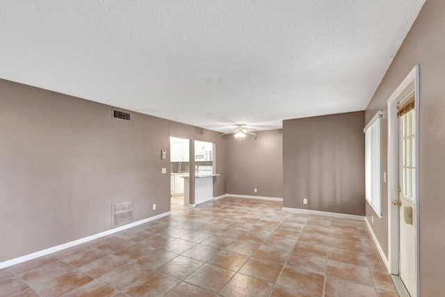 empty room with a textured ceiling, ceiling fan, baseboards, and light tile patterned flooring