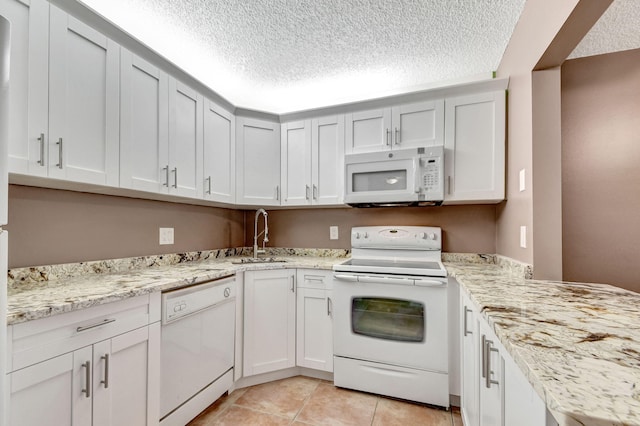 kitchen with white appliances, a sink, a textured ceiling, light tile patterned flooring, and light stone counters