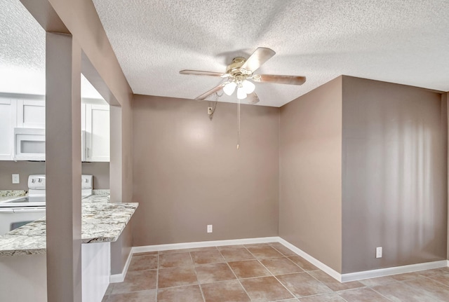 unfurnished dining area with a textured ceiling, a ceiling fan, light tile patterned floors, and baseboards