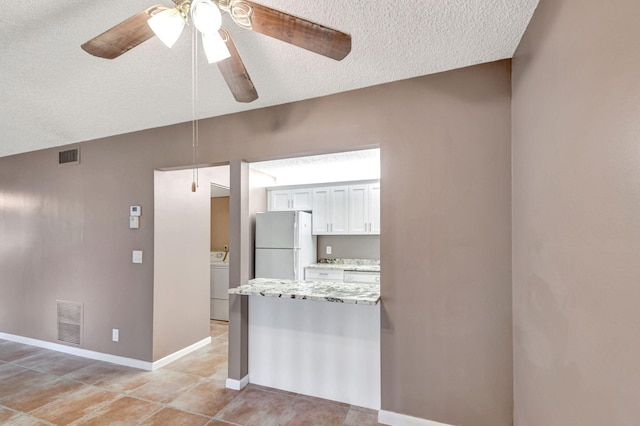 kitchen featuring freestanding refrigerator, a textured ceiling, washer / dryer, white cabinets, and a ceiling fan