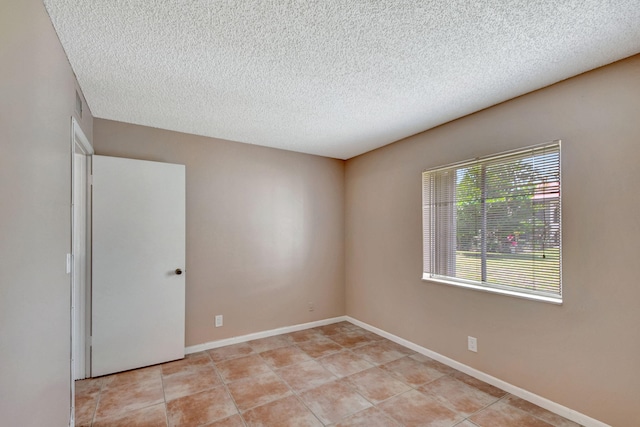 spare room with a textured ceiling, light tile patterned flooring, and baseboards