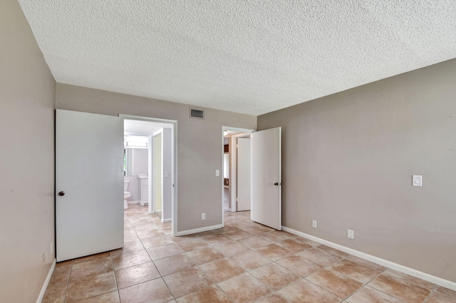unfurnished bedroom featuring a textured ceiling, light tile patterned floors, baseboards, and ensuite bathroom