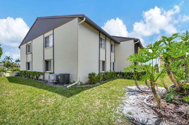 view of side of property featuring stucco siding, central AC, and a lawn