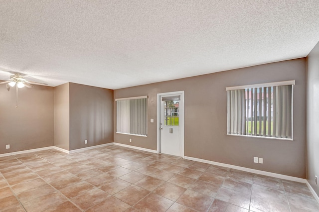 empty room with a ceiling fan, a textured ceiling, baseboards, and light tile patterned floors