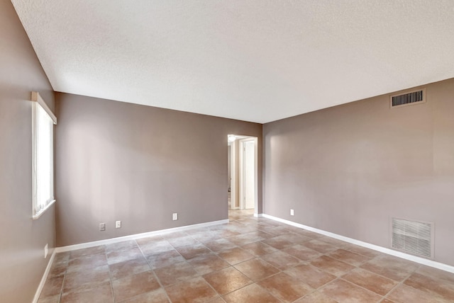 spare room featuring a textured ceiling, baseboards, and light tile patterned flooring