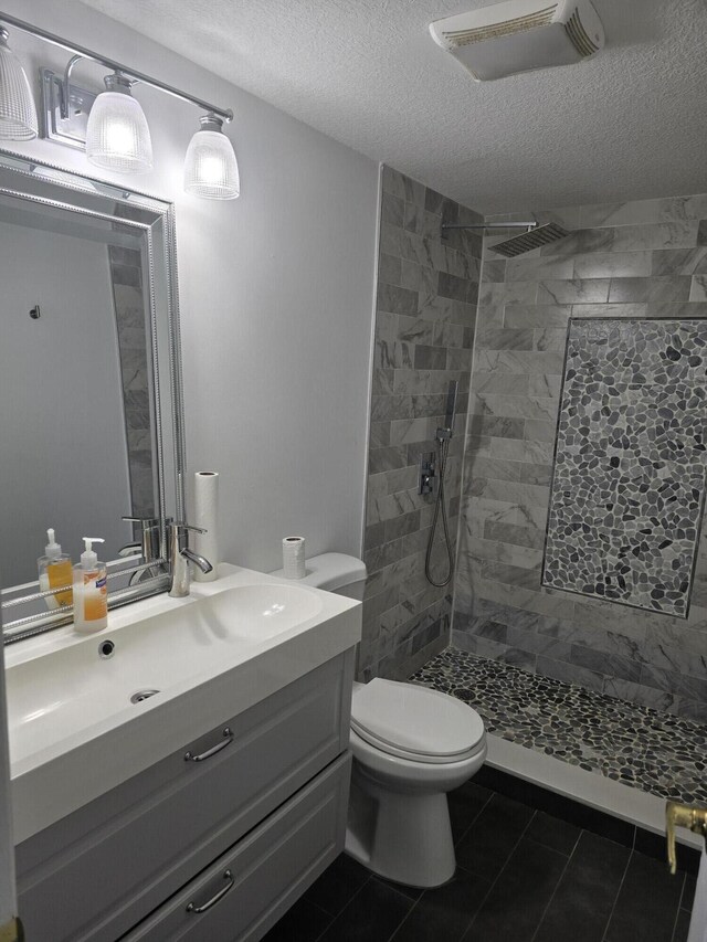 full bathroom featuring toilet, a textured ceiling, vanity, a tile shower, and tile patterned floors