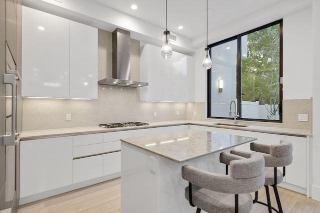 kitchen with wall chimney exhaust hood, a sink, modern cabinets, light wood-style floors, and recessed lighting