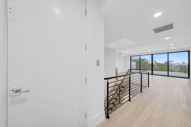 hall featuring an upstairs landing, floor to ceiling windows, recessed lighting, light wood-style flooring, and baseboards
