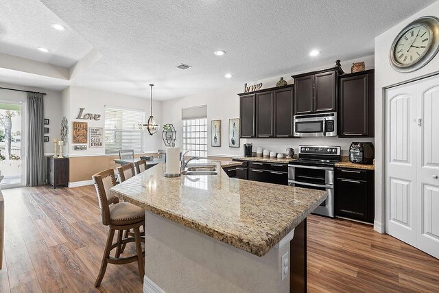 7267 Prudencia Dr, Lake Worth, FL 33463 - kitchen with stainless steel appliances, a sink, a textured ceiling, wood finished floors, and a breakfast bar