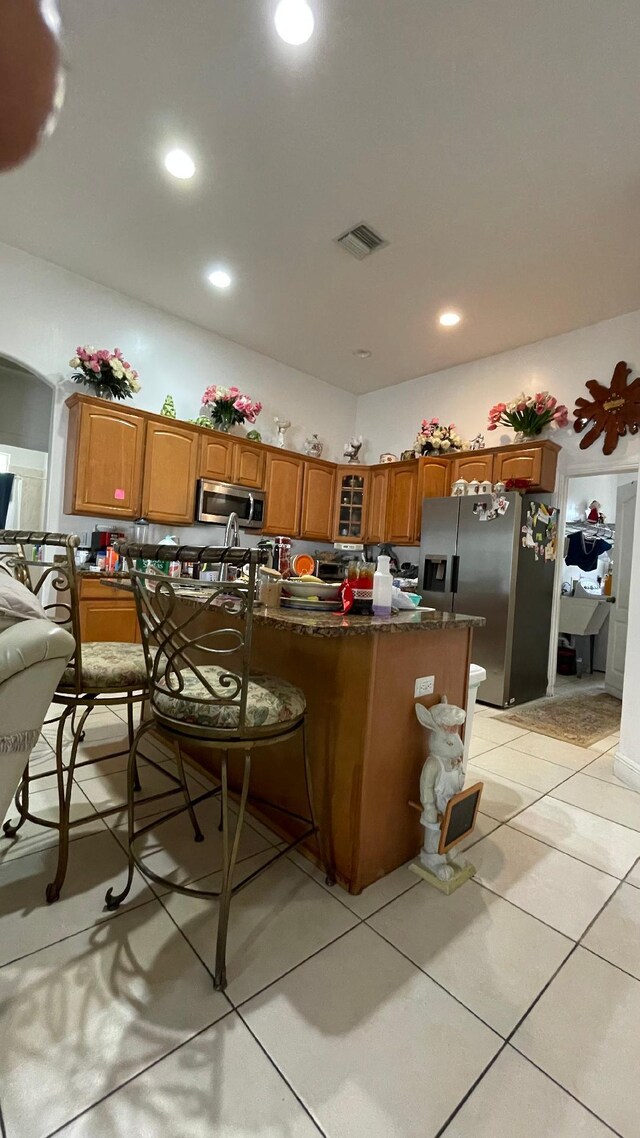2332 SW Savona Blvd, Port Saint Lucie, FL 34953 - kitchen featuring appliances with stainless steel finishes, brown cabinets, glass insert cabinets, light tile patterned floors, and a kitchen breakfast bar