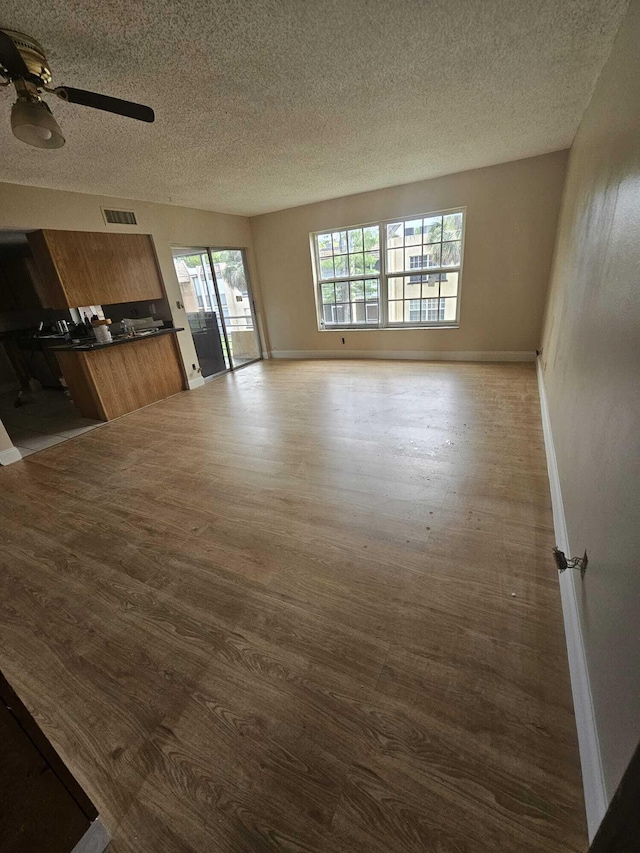 unfurnished living room with dark wood finished floors, a textured ceiling, a ceiling fan, and baseboards