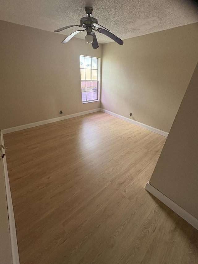 spare room featuring a textured ceiling, wood finished floors, ceiling fan, and baseboards