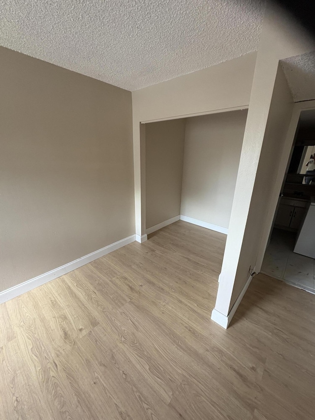 unfurnished room with wood finished floors, a textured ceiling, and baseboards