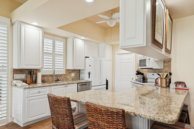 2596 Irma Lake Dr, West Palm Beach, FL 33411 - kitchen with white appliances, a sink, a breakfast bar, a peninsula, and white cabinetry