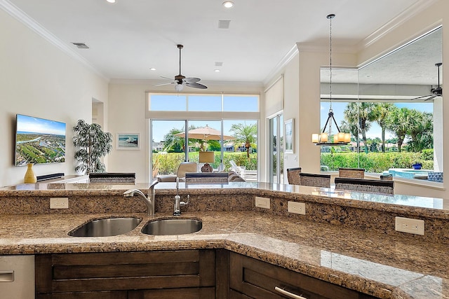 kitchen featuring ceiling fan, a sink, ornamental molding, stone countertops, and open floor plan