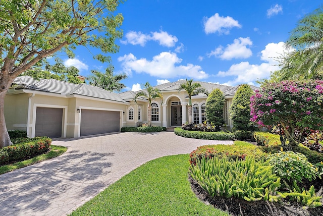 mediterranean / spanish-style home featuring an attached garage, decorative driveway, stucco siding, and a tile roof