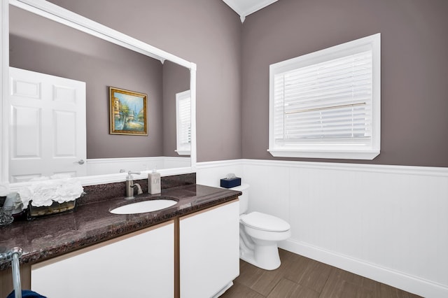 half bathroom featuring wainscoting, vanity, toilet, healthy amount of natural light, and wood finished floors