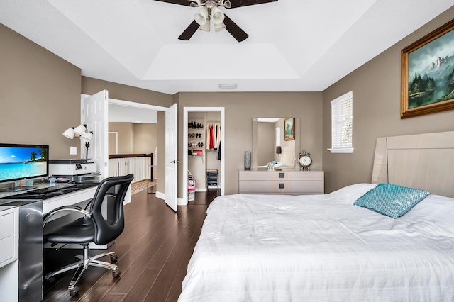 bedroom with a raised ceiling, dark wood finished floors, a walk in closet, an office area, and a closet