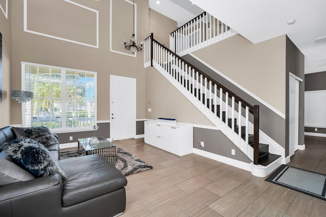 living room with stairs, a chandelier, baseboards, a high ceiling, and wood finished floors