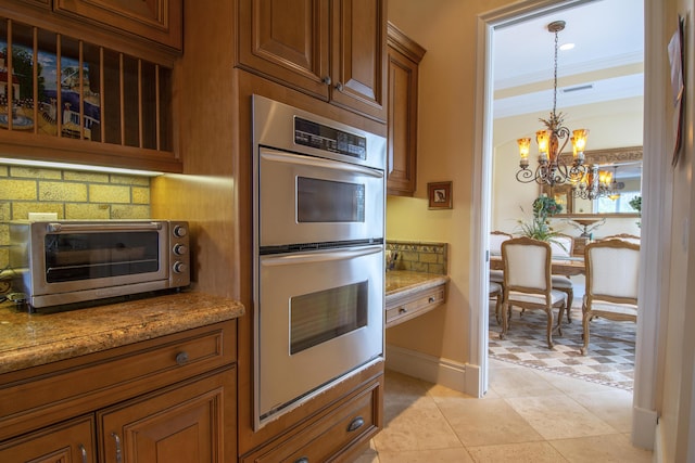 143 SE Bella Strano, Port Saint Lucie, FL 34984 - kitchen with stainless steel double oven, decorative backsplash, a chandelier, brown cabinetry, and hanging light fixtures