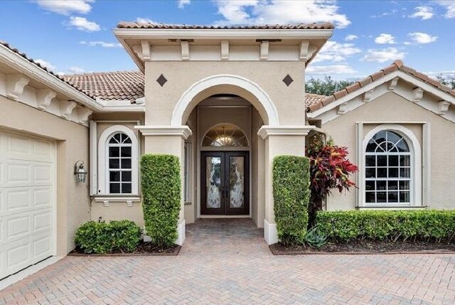 9400 Briarcliff Trce, Port Saint Lucie, FL 34986 - view of exterior entry with french doors, a tiled roof, stucco siding, a garage, and decorative driveway