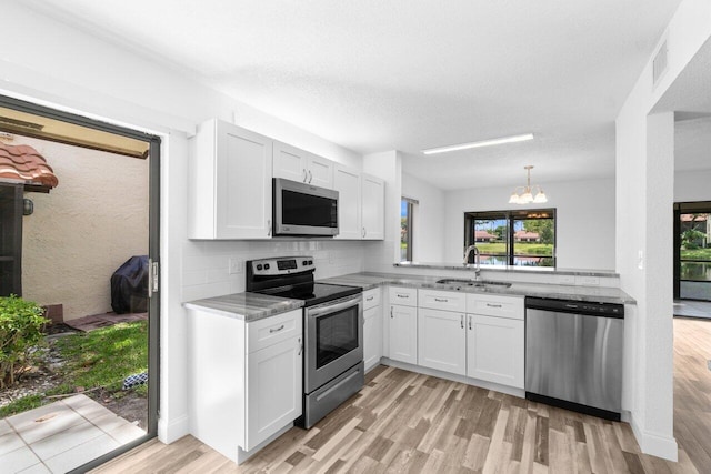 10679 Ocean Palm Way Unit 101, Boynton Beach, FL 33437 - kitchen with appliances with stainless steel finishes, a sink, light wood-type flooring, a chandelier, and white cabinets