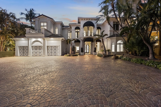 mediterranean / spanish-style house featuring a balcony, stucco siding, a garage, decorative driveway, and french doors