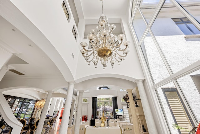 foyer featuring a chandelier, a towering ceiling, decorative columns, arched walkways, and ornamental molding