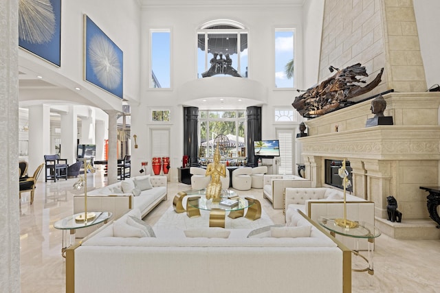 living room featuring a high ceiling, a fireplace, crown molding, and ornate columns