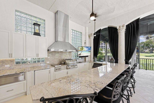 kitchen with wall chimney exhaust hood, a warming drawer, tasteful backsplash, light stone counters, and a textured ceiling