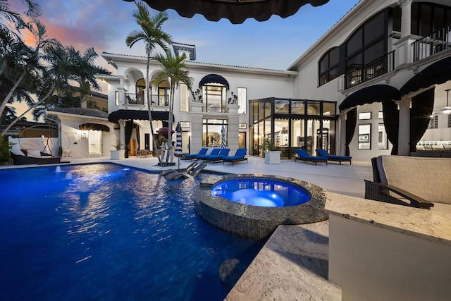 pool at dusk featuring a patio area and a pool with connected hot tub