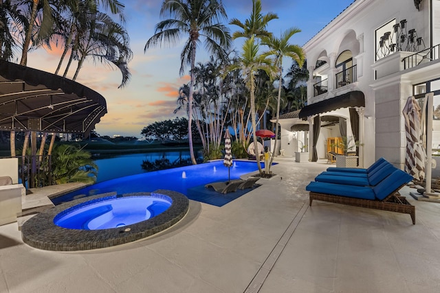 pool at dusk with a pool with connected hot tub, a patio area, and a water view
