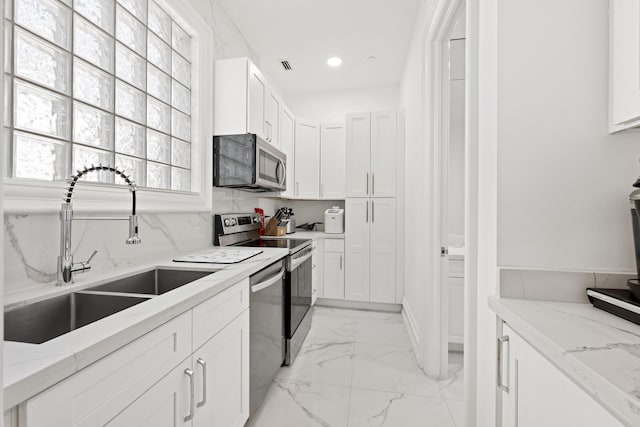 kitchen featuring appliances with stainless steel finishes, a sink, light marble finish flooring, white cabinets, and light stone counters