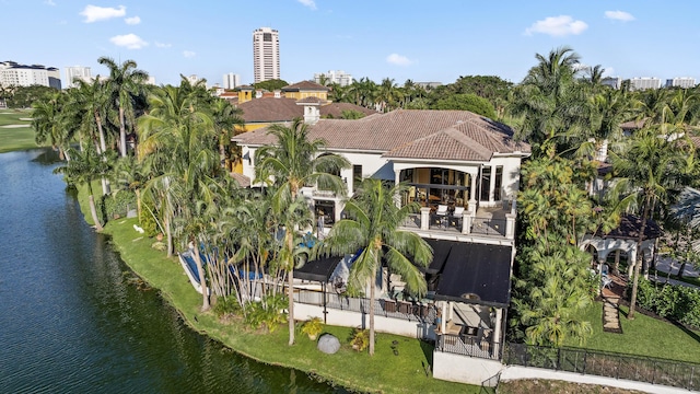 back of property with a balcony, a water view, and a tiled roof
