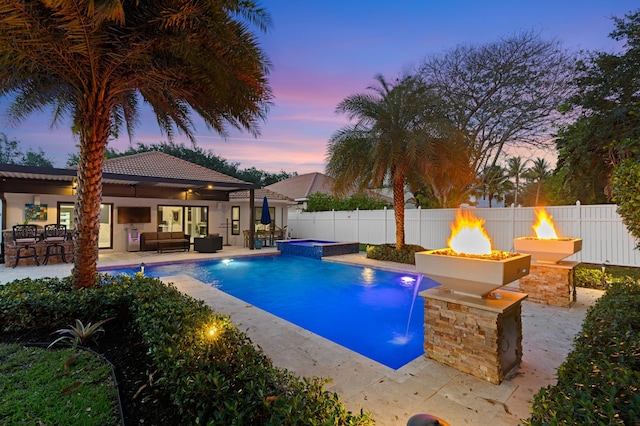 1010 Delray Lakes Dr, Delray Beach, FL 33444 - pool at dusk with an outdoor living space with a fire pit, a fenced backyard, a patio, and a pool with connected hot tub