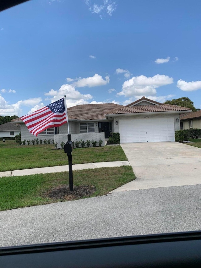 ranch-style home featuring a tile roof, an attached garage, a front yard, concrete driveway, and stucco siding
